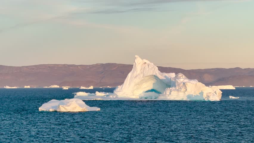 Experience the breathtaking coastal beauty of Baffin Island, where glistening icebergs meet serene waters against a backdrop of mountains at dawn.