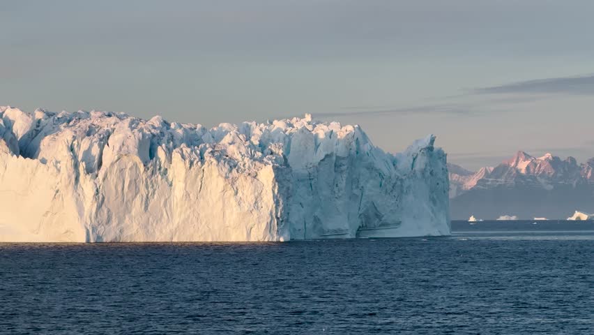 Experience the breathtaking coastal beauty of Baffin Island, where glistening icebergs meet serene waters against a backdrop of mountains at dawn.