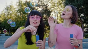 Girl friends blow soap bubbles near plaza smiling brightly. Couple follows floating spheres playing with bubble wand while cheerful mood grows in park - Powered by Shutterstock - Get 15% off with code: PIKWIZARD15