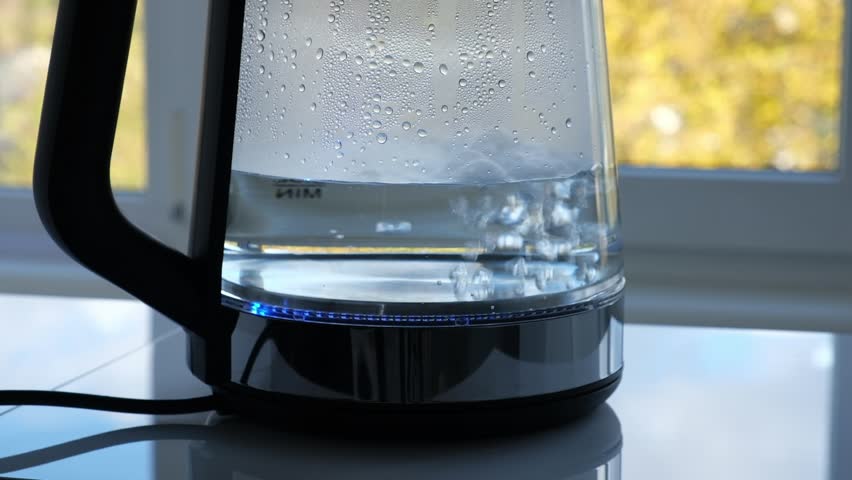 Hot water boiling in a kettle on a sunny kitchen countertop near a window