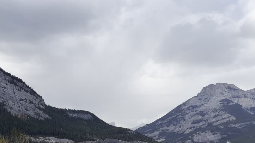 Scenic view of mountains and hills under cloudy sky on the road to Banff, Canada. Majestic Rocky Mountains landscape with moving clouds and dramatic light before the national park.