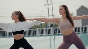 A yoga instructor is assisting a young woman with her Warrior II pose during an outdoor fitness class next to a swimming pool. Personal training and guidance focusing on form, health, and wellness - Powered by Shutterstock - Get 15% off with code: PIKWIZARD15