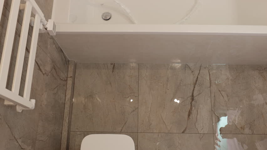 Bathroom flooding, plumbing failure, wet floor. Water leaking from bathtub flooding bathroom floor, with person stepping in water. Concept plumbing issue or home emergency.