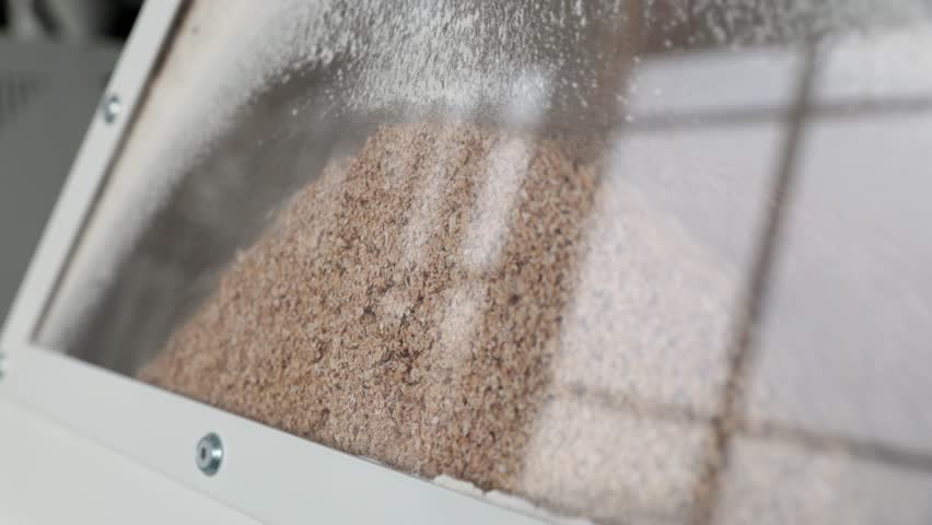 Rough wheat flour pours into container with clear plastic window in modern mill