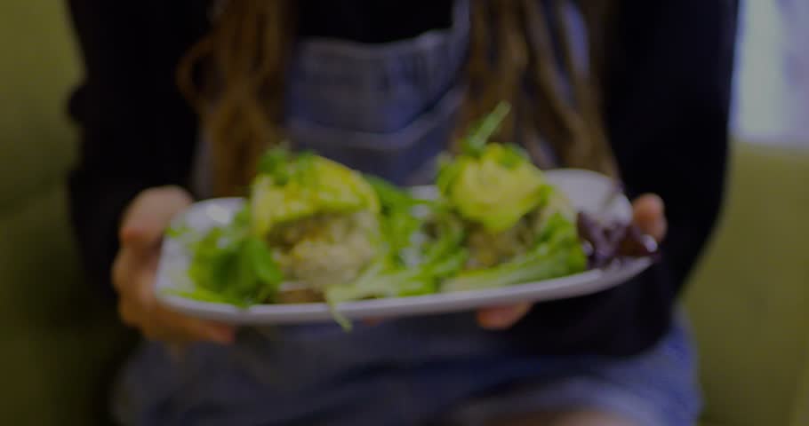 Handheld plate with gourmet avocado toast topped with avocado rose, microgreens, and fresh greens. Creative plant-based brunch, healthy vegan food, shown served by a person for cafe lifestyle themes.