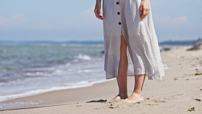 Loving young couple embraces on sandy shore of Baltic Sea with soft waves at their feet. Woman in white lifts slightly as they hug, creating tender and intimate moment under clear daylight