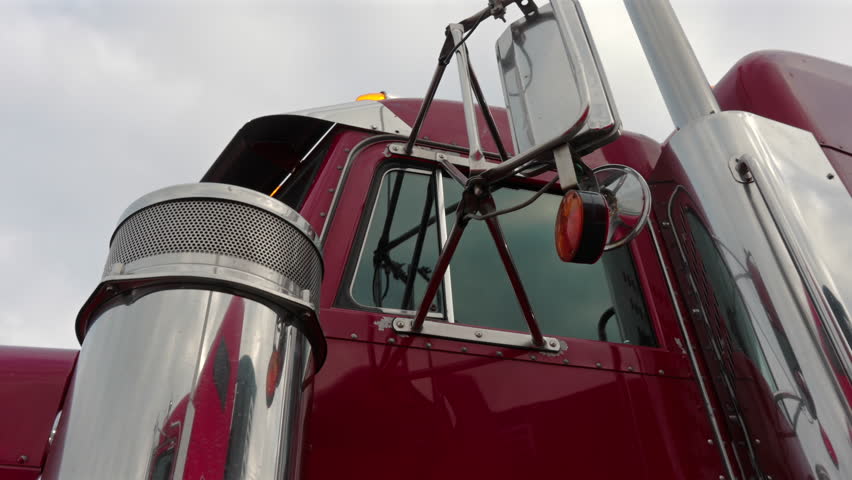 A red truck is shown up close, highlighting its shiny side mirror and details under natural light during the day.