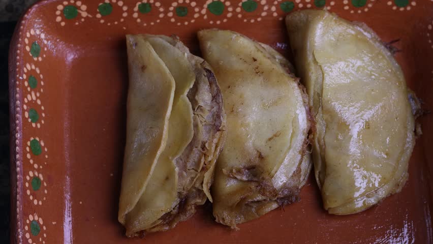 Hands preparing delicious traditional steamed tacos with spicy red sauce in a clay dish