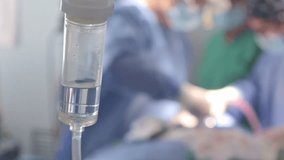 A close-up of an intravenous drip with surgeons working in the blurred background. The image represents the delicate balance of life support and medical precision within a sterile surgical environment - Powered by Shutterstock - Get 15% off with code: PIKWIZARD15