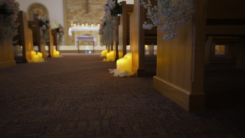 The aisle with flower and candle decorated wooden pews rows in empty church. Christian cathedral interior decoration for the wedding event