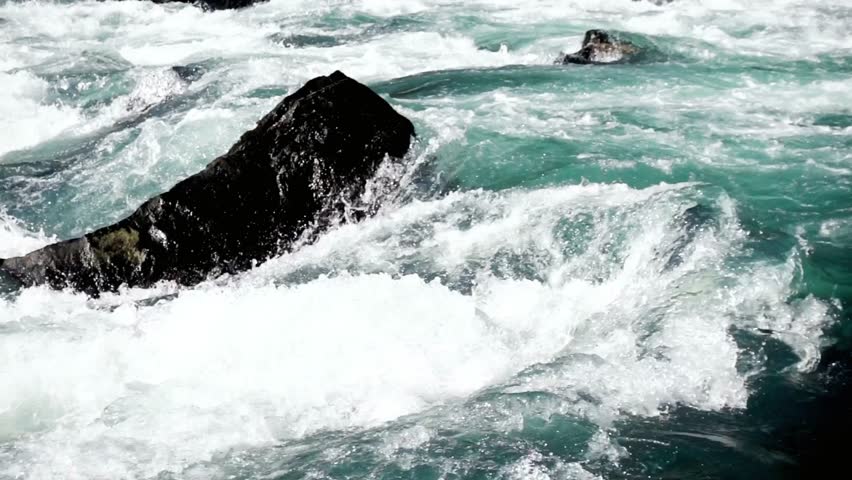 Rushing river water crashing against a dark rock creating white water rapids scene