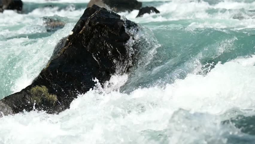 Rushing river water crashing against a dark rock creating white water rapids