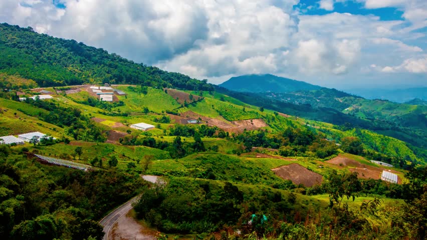 Lush green mountain landscape with terraced fields under a bright cloudy sky