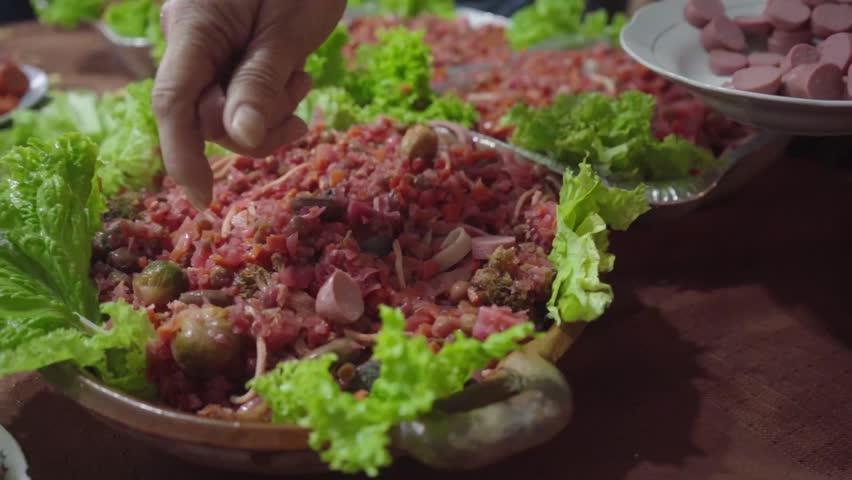 Finishing the preparation of fiambre plate with cold cuts and hand-placed sausage on a clay dish