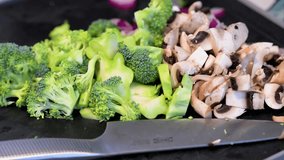 Freshly chopped broccoli, mushrooms, and red onions are prepped on a dark cutting board. A knife rests in the foreground, ready for healthy cooking and meal preparation. - Powered by Shutterstock - Get 15% off with code: PIKWIZARD15