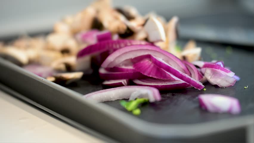 Sliced red onions, a key aromatic for many recipes, are in sharp focus. This culinary close-up shows healthy ingredients being prepped for a delicious, home-cooked meal.