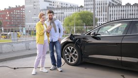 A couple looks at a phone while their electric vehicle charges in an urban setting. - Powered by Shutterstock - Get 15% off with code: PIKWIZARD15