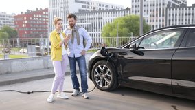 A couple discusses while their electric vehicle charges in an urban setting, using a smartphone. - Powered by Shutterstock - Get 15% off with code: PIKWIZARD15