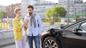 A couple looks at a smartphone while their electric vehicle charges at a charging station. - Powered by Shutterstock - Get 15% off with code: PIKWIZARD15