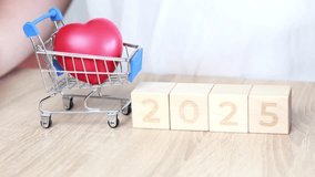 A hand places wooden blocks showing 2026 next to a mini shopping cart holding a red heart. This scene captures themes of love, future planning, and optimism - Powered by Shutterstock - Get 15% off with code: PIKWIZARD15