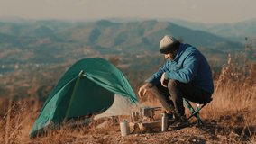 Traveler preparing coffee on a small gas burner near a tent with mountain scenery in the background. Outdoor adventure lifestyle, peaceful camping moment, authentic travel experience. - Powered by Shutterstock - Get 15% off with code: PIKWIZARD15