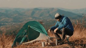 Traveler preparing coffee on a small gas burner near a tent with mountain scenery in the background. Outdoor adventure lifestyle, peaceful camping moment, authentic travel experience. - Powered by Shutterstock - Get 15% off with code: PIKWIZARD15