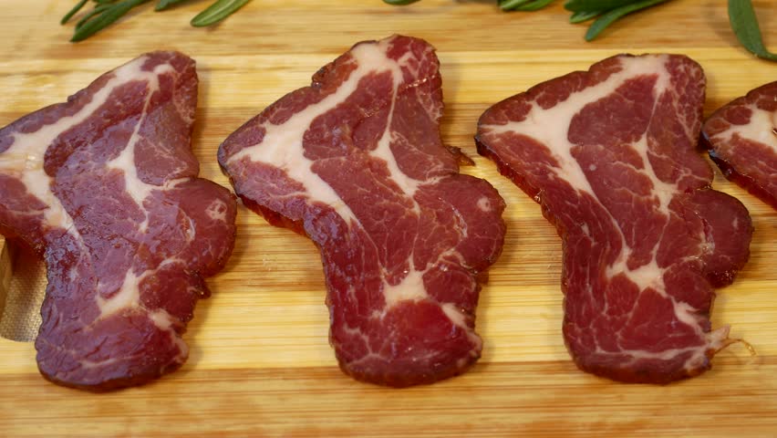 Thinly sliced cured meat pieces on a wooden board. Concept of nutritious and delicious meat dishes, protein-rich diet, and traditional cuisine