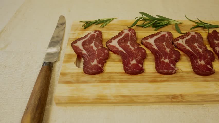 Thinly sliced pieces of cured meat on a wooden board. Knife nearby. Concept of nutritious and tasty meat dishes, protein-rich diet and traditional cuisine
