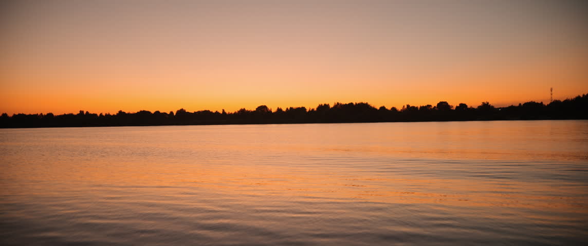 Breathtaking Sunset Over Tranquil Waters: A Serene Landscape Depicting the Gentle Transition of Day to Night with Vibrant Orange and Blue Sky Reflections