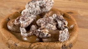 Close-up of a delicious cookie topped with caramel, cream, and sugared pecan, displayed on a rotating wooden plate with an orange background. - Powered by Shutterstock - Get 15% off with code: PIKWIZARD15