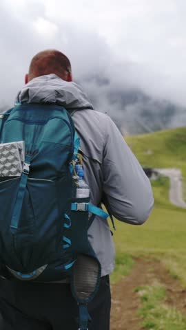 Back view of hiker walking uphill with backpack in the Dolomites