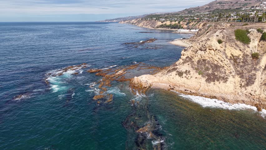 Aerial drone shot of rocky California shoreline with waves rolling onto cliffs and tide pools.