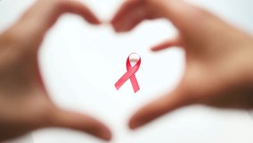 Close-up of pink awareness ribbon on white softly blurred heart-shaped hands in foreground, symbolizing love and support during Breast Cancer Awareness Month. - Powered by Shutterstock - Get 15% off with code: PIKWIZARD15