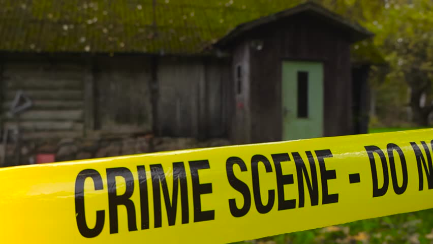 Crime scene police yellow forensic investigation tape ribbon in front of an old farm house or a shed barn in autumn green garden, fallen leaves, moss covering the roof. Entrance.