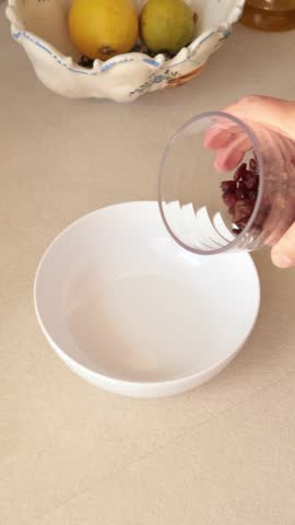 Anonymous person pours dried raisins into bowl. Cooking and healthy eating.