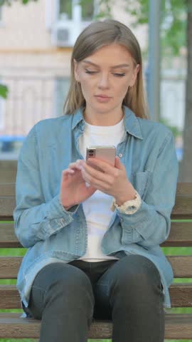 Woman Using Smartphone while Sitting on Bench in Park, Vertical Video