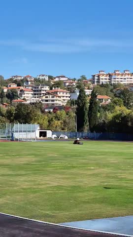 Stadium lawn care. Football pitch maintenance. Green grass. A man on a special tractor tends the football pitch.
