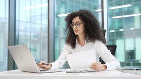 Busy focused businesswoman is doing paperwork using a laptop computer while sitting at workplace in business office. Thoughtful female financier deals with financial report, engaged in accounting - Powered by Shutterstock - Get 15% off with code: PIKWIZARD15