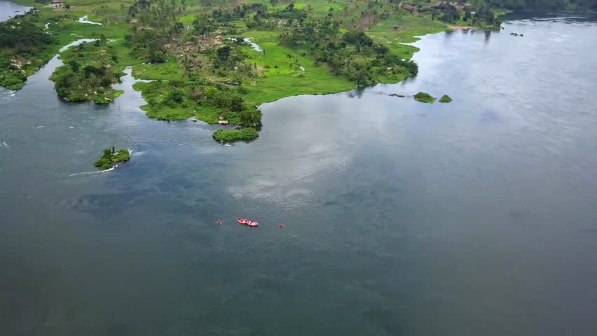 High aerial orbit over white water rafting on the Nile River near Jinja, Uganda as Red rafts navigate swirling currents and green islands in Africa’s iconic adventure corridor.