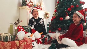 Two people in Santa hats open a glowing gift beside a decorated Christmas tree and fireplace, surrounded by wrapped presents, stockings, and festive decor in a cozy home setting. - Powered by Shutterstock - Get 15% off with code: PIKWIZARD15