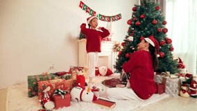 Festive living room with two people mom and daughter in Santa hats exchanging gifts beside a decorated Christmas tree, surrounded by wrapped presents, ornaments, and a fireplace mantel. - Powered by Shutterstock - Get 15% off with code: PIKWIZARD15