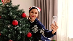 Smiling person in a Santa hat takes a selfie beside a decorated Christmas tree at home, wearing a cozy snowflake sweater and enjoying a festive holiday moment indoors. - Powered by Shutterstock - Get 15% off with code: PIKWIZARD15