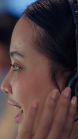 Close-up view of Asian woman wearing headset and smiling while talking in call center office, working as customer service representative.