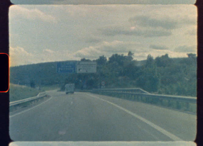 Vintage highway footage showing a vehicle driving on a Spanish road with directional signs to Girona and Barcelona under a cloudy sky