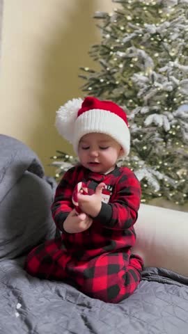 Adorable baby in festive outfit by Christmas tree.