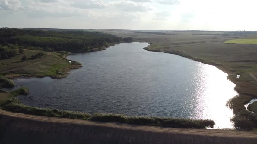 Aerial footage of a calm, dark-blue pond (reservoir) nestled in the wide, green valleys of the Donetsk region, Eastern Ukraine.