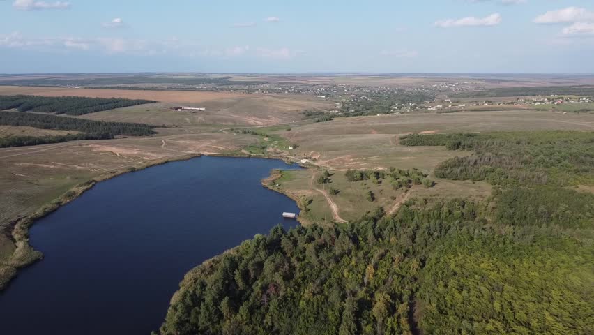 Aerial footage of a calm, dark-blue pond (reservoir) nestled in the wide, green valleys of the Donetsk region, Eastern Ukraine.