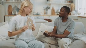Spouses discussing buying house woman holding house symbol, man with money. Interracial marriage and dream of own home, save money for mortgage, multiethnic loving couple sitting in new apartment - Powered by Shutterstock - Get 15% off with code: PIKWIZARD15