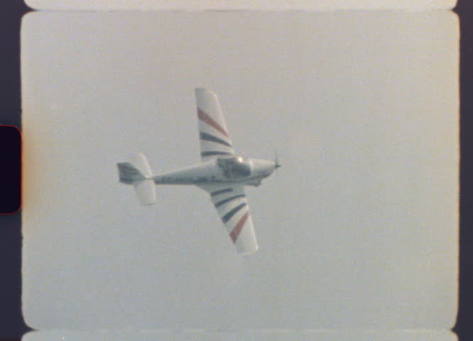 A small vintage stunt aircraft flies across the sky executing dynamic aerial maneuvers captured on real 8mm film with visible grain and nostalgic atmosphere