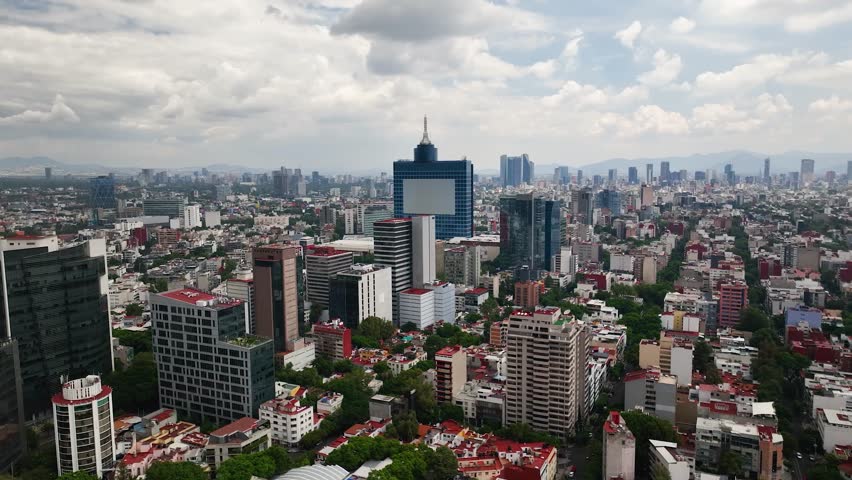 Drone traveling shot above Colonia del Valle in Mexico City. World Trade Center stands out amid dense skyline, leafy streets, famous avenues, small parks under cloudy daylight—clean, cinematic.